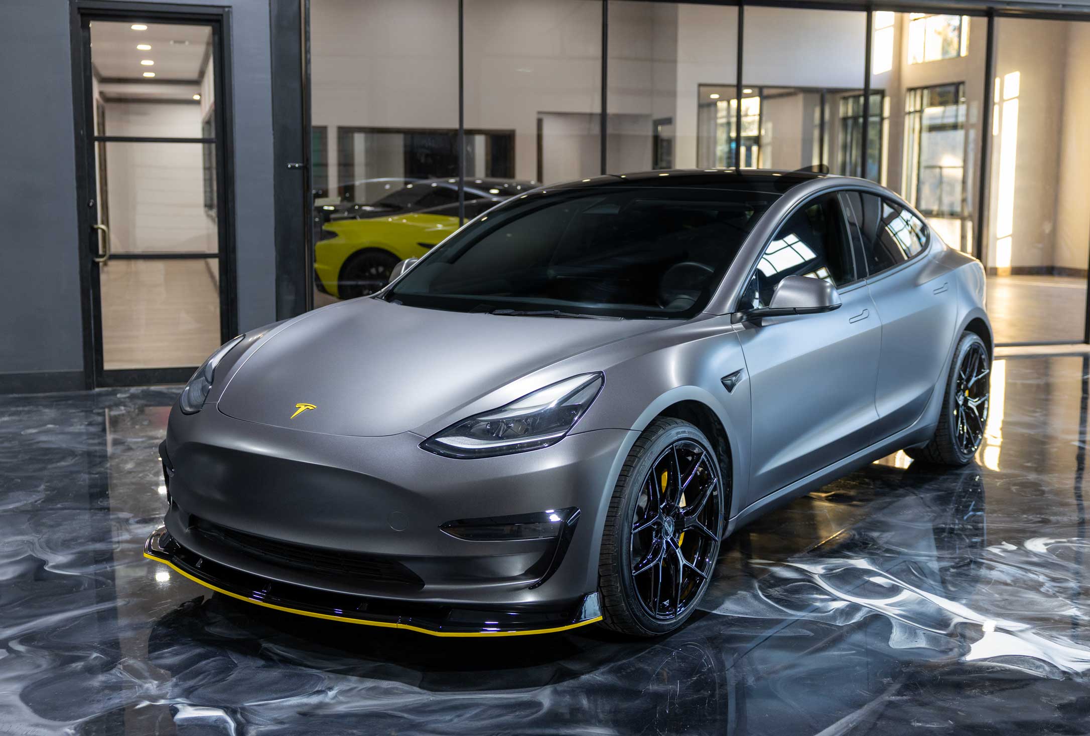 Custom Tesla showcased inside the Apex Custom Innovations Dallas showroom featuring vinyl wrap, upgraded wheels and tires, and a performance-inspired body kit